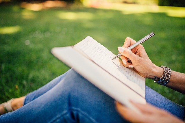 woman sat on grass, writing in a notebook